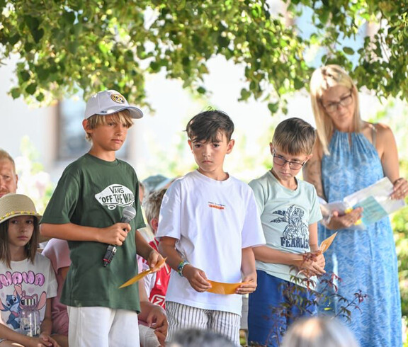 Kinder tragen unter einem schattigen Baum Beiträge beim Sommerfest im Haus Maria vor.