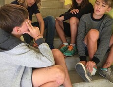 Mehrere Kinder sitzen auf einer Treppe im Schulgebäude, tauschen sich aus und verbringen gemeinsam Zeit im Rahmen einer Gruppenaktivität.