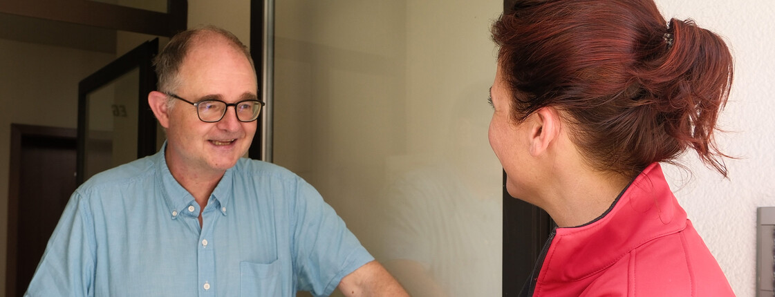 Zwei Personen am Hauseingang, eine mit roter Caritas-Jacke, übergibt Spendeninfos an Bewohner.