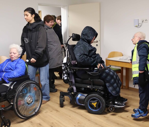 Zwei Personen im Rollstuhl und zwei weitere in einem neuen Haus.