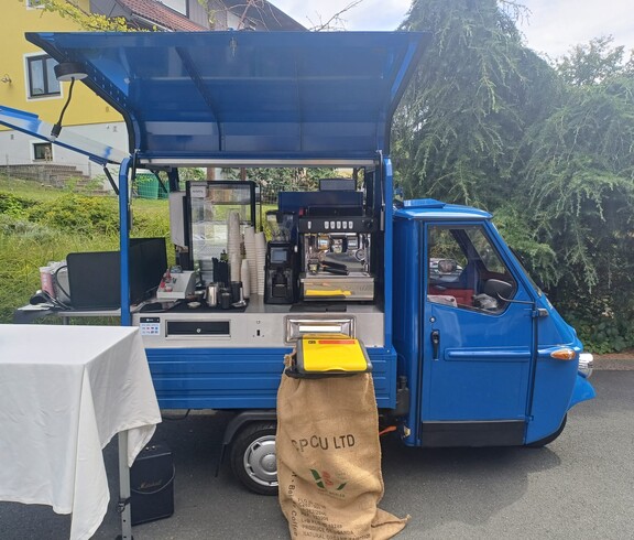 Ein blauer Kaffeewagen steht im Außenbereich des Pflegewohnhauses und ist mit einer Kaffeemaschine, Bechern und Zubehör für die Bewirtung der Gäste ausgestattet.