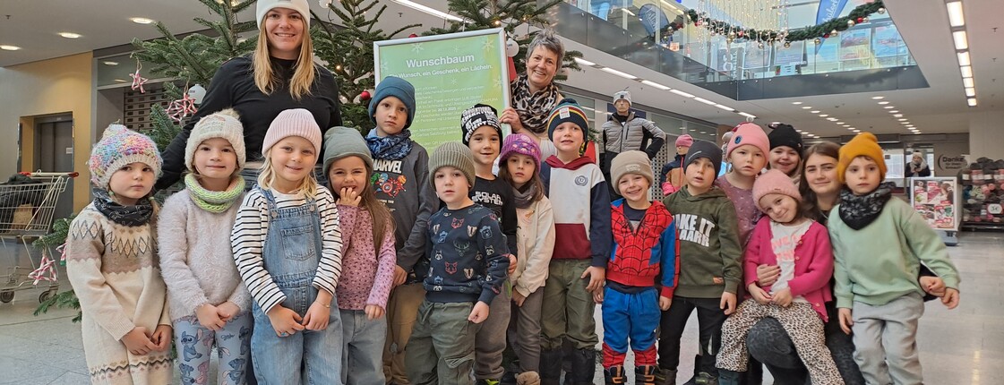 Eine Gruppe Kindergartenkinder steht vor einem Christbaum in einem Einkaufscenter.