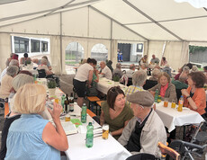 Zahlreiche Gäste sitzen an gedeckten Tischen im Festzelt und verbringen den Nachmittag gemeinsam.