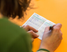 Eine Person, die grün bekleidet ist, trägt in ein Trinktagebuch ein. 