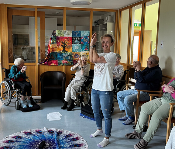 Gemeinsame Dehnübung mit seitlichem Armheben bei einer Seelenyoga-Stunde mit Senior*innen.
