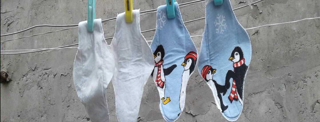 Mehrere bunte, selbst genähte Stoffbinden mit Pinguinmotiven hängen an einer Wäscheleine vor einer grauen Betonwand zum Trocknen.