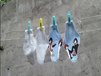 Mehrere bunte, selbst genähte Stoffbinden mit Pinguinmotiven hängen an einer Wäscheleine vor einer grauen Betonwand zum Trocknen.
