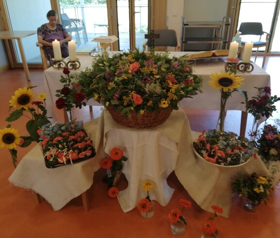 Blumen, Kerzen und Altartisch im Raum dekoriert mit Kräutersträußen und Sonnenblumen