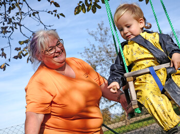 Eine kleines Mädchen sitzt auf dem Schoß einer Frau. Vor ihnen liegt ein Buch am Tisch, das sie sich gemeinsam ansehen.