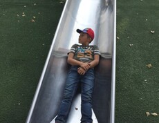 Ein Kind liegt auf einer breiten Metallrutsche auf einem Spielplatz im Donaupark und genießt eine Pause beim Spielen.