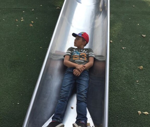 Ein Kind liegt auf einer breiten Metallrutsche auf einem Spielplatz im Donaupark und genießt eine Pause beim Spielen.