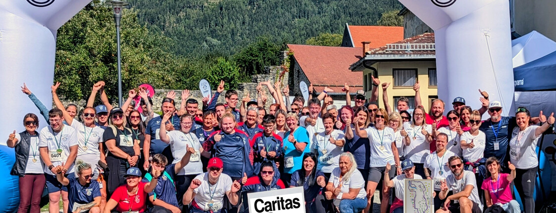 Große Gruppe von Teilnehmenden und Unterstützer*innen vor dem Caritas-Startbogen in Friesach.