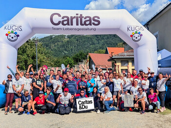 Große Gruppe von Teilnehmenden und Unterstützer*innen vor dem Caritas-Startbogen in Friesach.