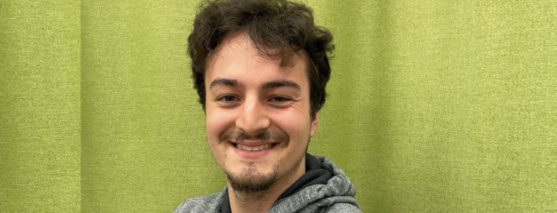 Junger Mann vor grünem Hintergrund lächelt in die Kamera.