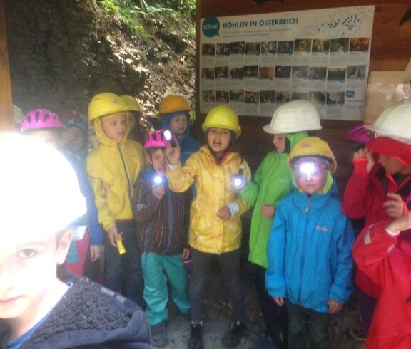 Kinder tragen Helme und Stirnlampen bei einer Höhlenexkursion und erhalten Informationen über die Erforschung von Höhlen in Österreich.