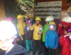 Kinder tragen Helme und Stirnlampen bei einer Höhlenexkursion und erhalten Informationen über die Erforschung von Höhlen in Österreich.