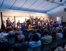 Eine Gruppe Musiker steht auf einer Bühne, ein Moderator hält ein Mikrophon