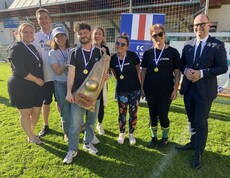 Sechs Personen stehen am Spielfeld und ein Mann hält den Pokal in den Händen.