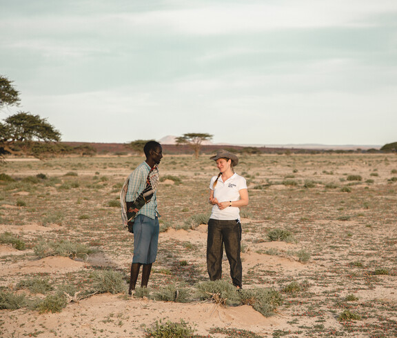 Caritas-Projektreferentin Theresa Sacher steht mit einem Mann in einer trockenen Landschaft in Marsabit und spricht mit ihm. Das Gespräch dreht sich um die Auswirkungen des Klimawandels auf die Lebensgrundlagen der Menschen.
