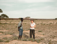 Caritas-Projektreferentin Theresa Sacher steht mit einem Mann in einer trockenen Landschaft in Marsabit und spricht mit ihm. Das Gespräch dreht sich um die Auswirkungen des Klimawandels auf die Lebensgrundlagen der Menschen.