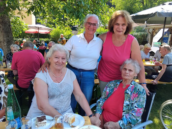Bewohner*innen und Angehörige versammeln sich beim Grillfest an einer gedeckten Festtafel im Garten.