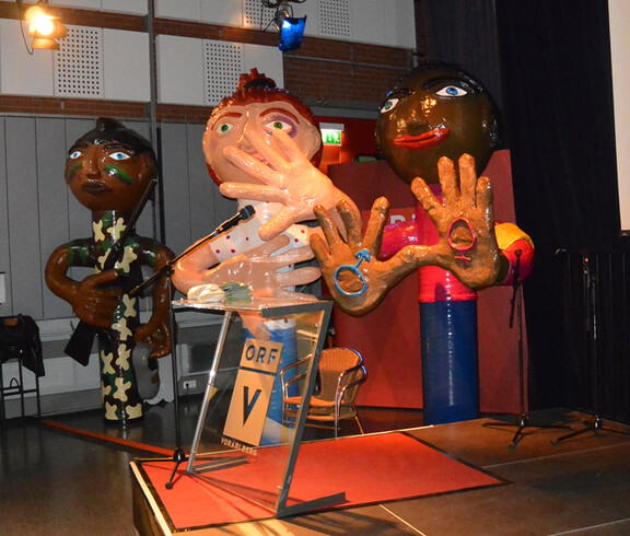 Ca. 2 Meter hohe Figuren stehen in einem größeren Saal. Sie repräsentieren Menschen unterschliedlicher Ehtnien. Im Vordergrund befindet sich eine Bühne. 