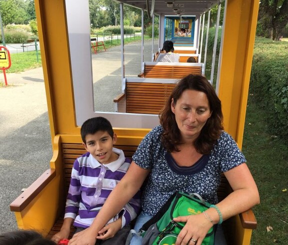 Eine erwachsene Begleitperson und ein Kind sitzen in einem Wagen der Parkeisenbahn und fahren gemeinsam durch den Donaupark.
