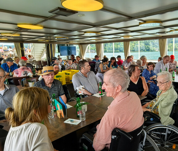 Reisegruppe von Haus Klara sitzt an Tischen auf einem Schiff und fährt über den Wörthersee.