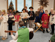 Kindergruppe in Kostümen spielt Adventsszene, Person mit Gitarre begleitet