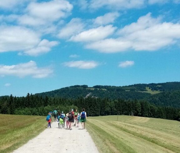 Kindergruppe wandert auf einem breiten Weg durch eine hügelige Landschaft und erkundet während der Projektwoche die Natur.