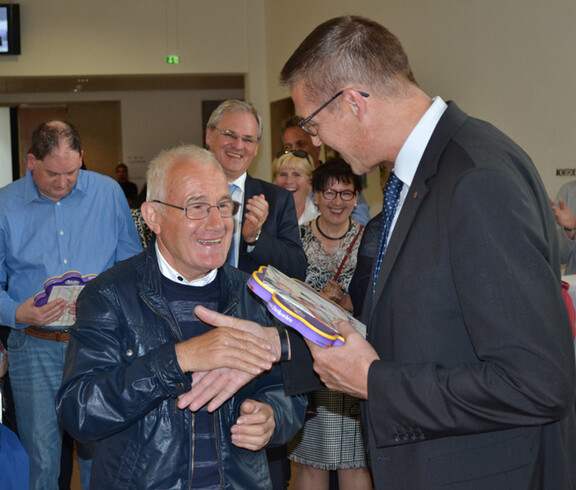 Landesrat Christian Bernhard gratuliert einem älteren Herrn und überreicht ihm eine Schokolade. 