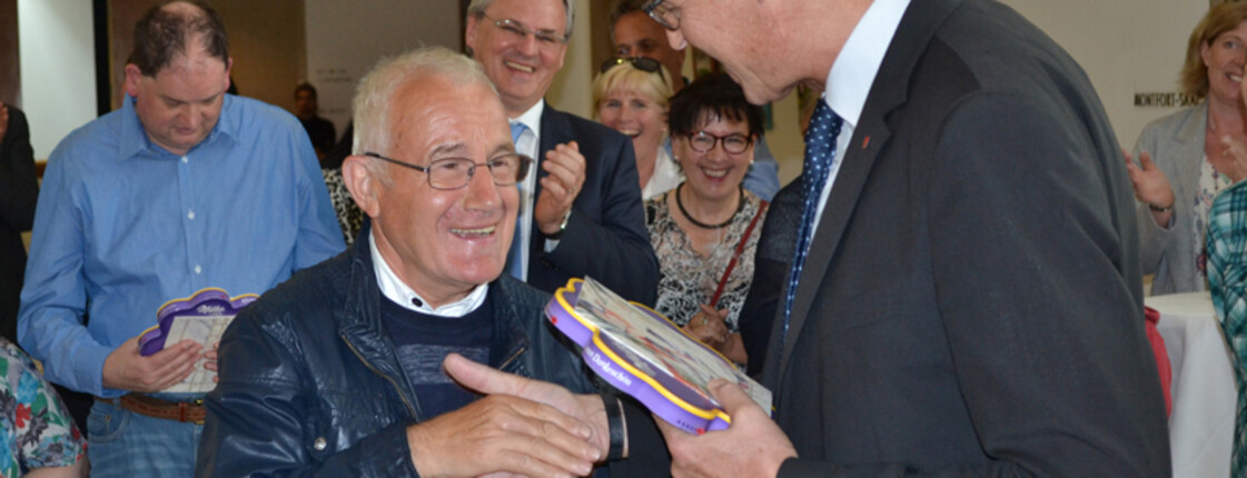 Landesrat Christian Bernhard gratuliert einem älteren Herrn und überreicht ihm eine Schokolade. 