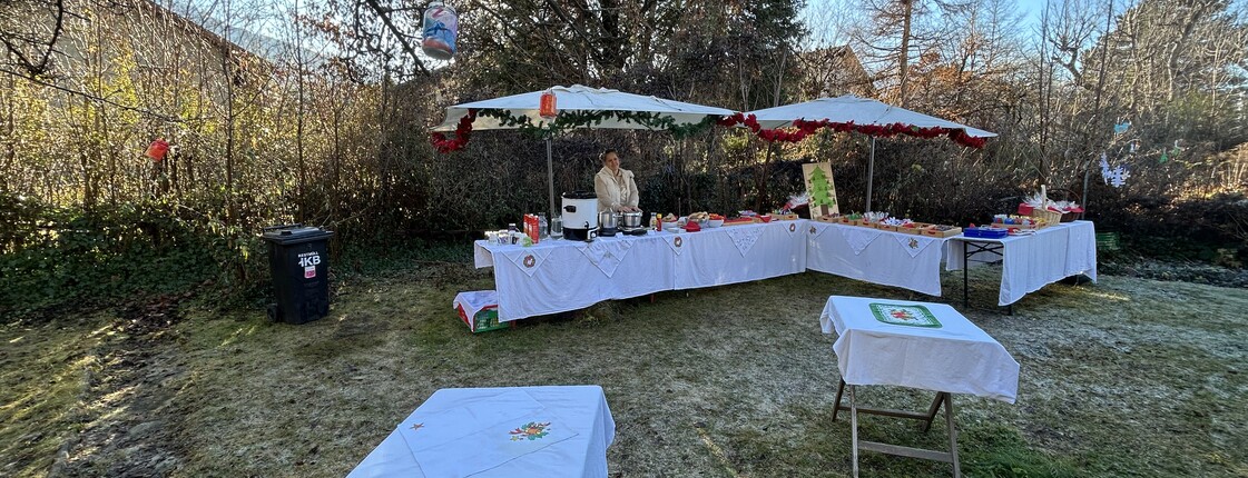 In einem Garten sind Tische mit weißen Tischdecken als Verkaufsstände aufgebaut.