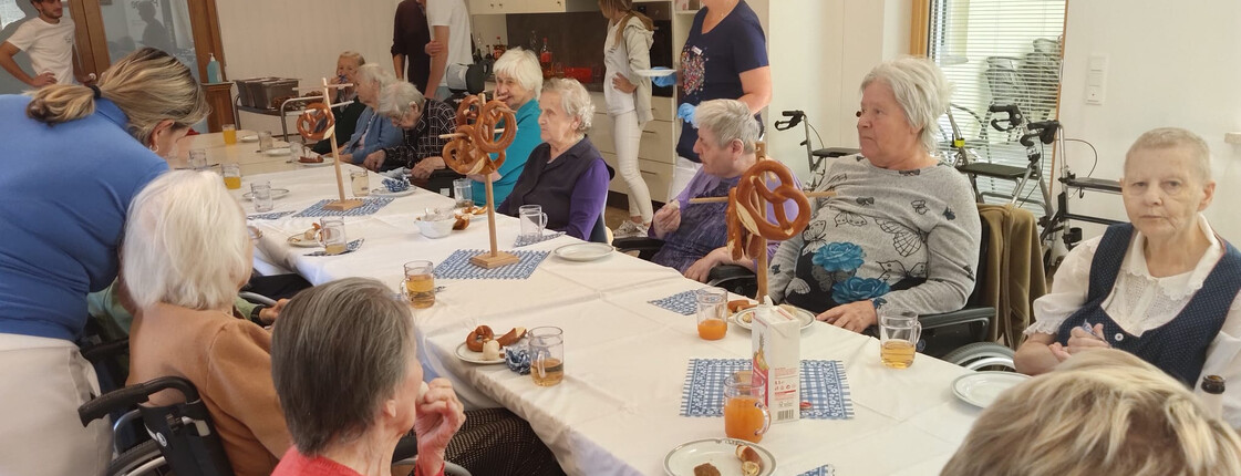 Bewohner*innen sitzen gemeinsam an einer festlich gedeckten Tafel mit Brezen und Saft.