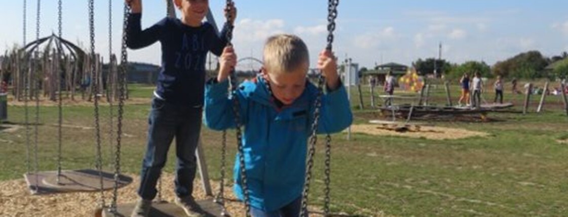 Kinder balancieren auf hängenden Trittplatten einer Motorikstation im Freien und trainieren spielerisch Gleichgewicht und Koordination.