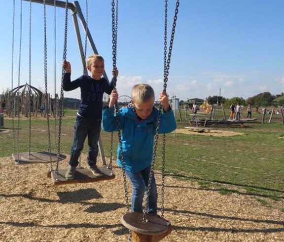 Kinder balancieren auf hängenden Trittplatten einer Motorikstation im Freien und trainieren spielerisch Gleichgewicht und Koordination.