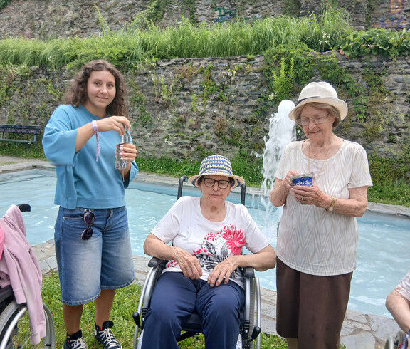 Bewohnerinnen und Schülerinnen machen gemeinsam Pause an einem Brunnen im Park.