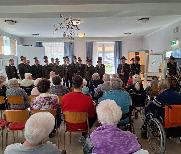 Männerchor in Tracht singt vor älteren Bewohner*innen im Veranstaltungssaal