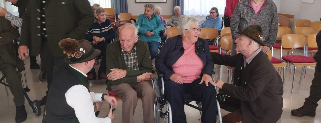 Senior*innen im Gespräch mit Jagdhornbläsern in traditioneller Tracht im Pflegewohnhaus