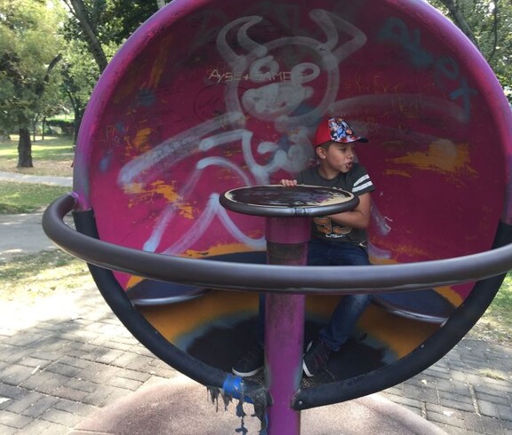 Ein Kind sitzt in einem runden Spielgerät auf einem Spielplatz im Donaupark und erkundet die Anlage im Freien.