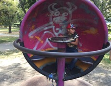 Ein Kind sitzt in einem runden Spielgerät auf einem Spielplatz im Donaupark und erkundet die Anlage im Freien.