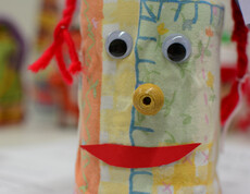 Eine Figur, die aus einem Glas gemacht ist, hat zwei Kulleraugen, einen roten Mund aus Papier und eine gelbe, schneckenartige Nase.