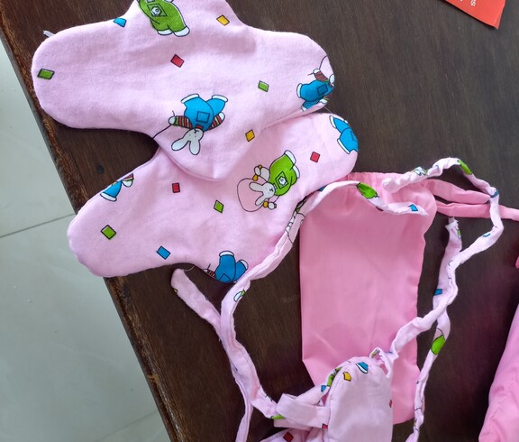 Zwei fertig genähte, rosafarbene Stoffbinden mit buntem Hasenmuster liegen auf einer Holzoberfläche; die Bindebänder sind deutlich sichtbar.