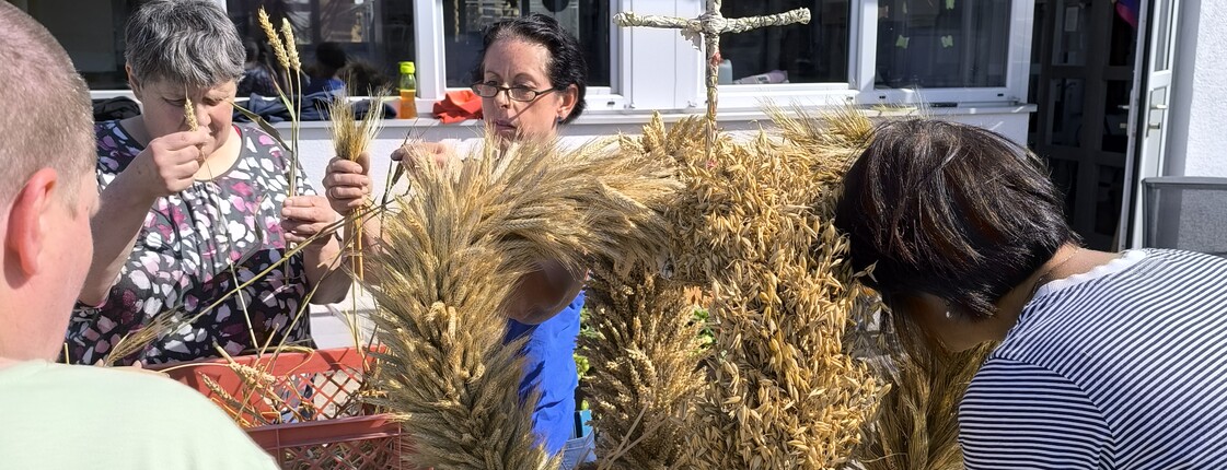 Eine Erntekrone steht im Freien auf einem Biertisch und wird noch von einer Frau geschmückt.