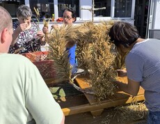 Eine Erntekrone steht im Freien auf einem Biertisch und wird noch von einer Frau geschmückt.