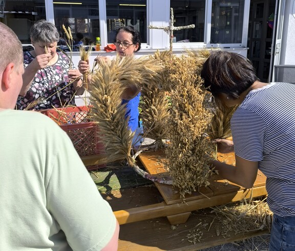 Eine Erntekrone steht im Freien auf einem Biertisch und wird noch von einer Frau geschmückt.