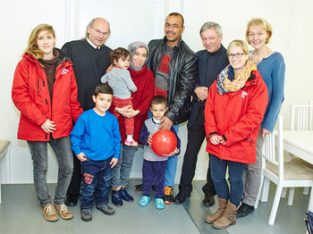 Drei Caritas-Mitarbeiterinnen, der Direktor der Caritas St. Pölten und ein Geistlicher mit einer Flüchtlingsfamilie im Containerdorf in Melk