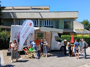 Viele Menschen stehen vor einem kleinen Bus, in dem es viele Informationen zum Thema psychische Gesundheit gibt. 