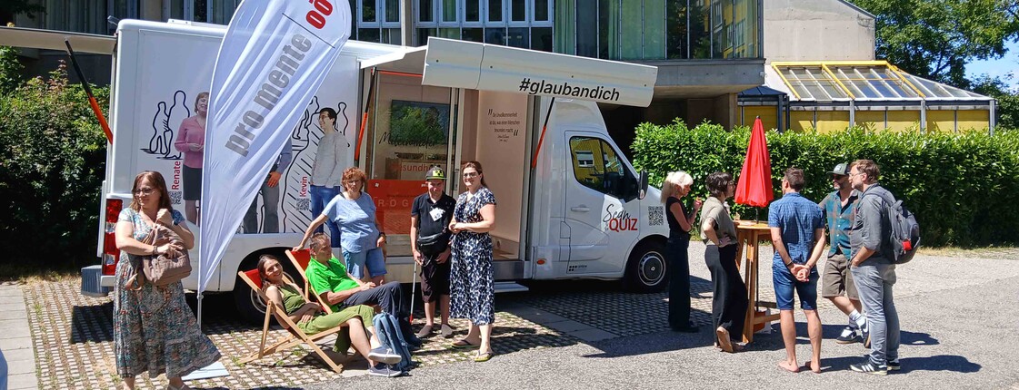 Viele Menschen stehen vor einem kleinen Bus, in dem es viele Informationen zum Thema psychische Gesundheit gibt. 