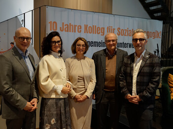5 Personen stehen vor einerm Jubiläumsplakat